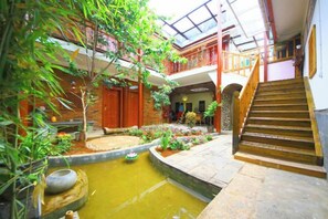 A multi-level atrium with a central water feature, wooden stairs, and a variety of plants. - Gudao Gudao Renjia Inn (Lijiang)
