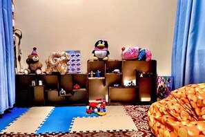 A room with a blue mat, a bean bag, shelves with various items, and a toy train. - Gudao Gudao Renjia Inn (Lijiang)