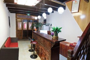 A reception area with a wooden counter, bar stools, and a red cushioned bench. - Gudao Gudao Renjia Inn (Lijiang)