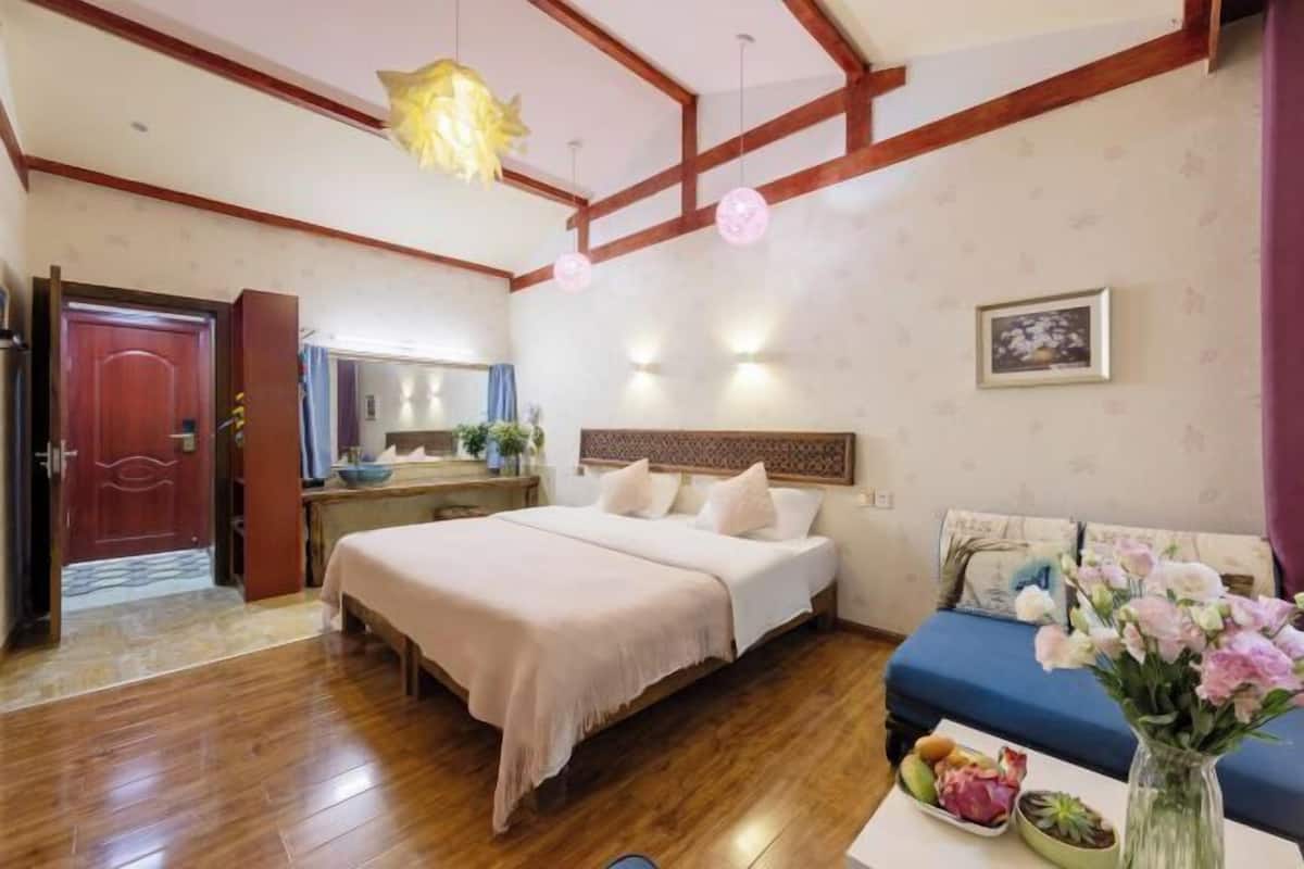 Een slaapkamer met een bed, een bank, een nachtkastje met een bloevas en een houten plafond.