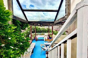 Un espacio exterior techado con piso azul, una cama y una silla.