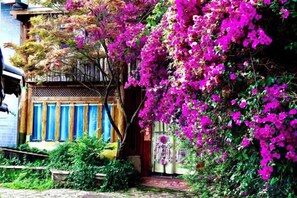 A traditional building with a wooden facade and a balcony, surrounded by lush greenery and vibrant pink bougainvillea flowers. - Gudao Gudao Renjia Inn (Lijiang)
