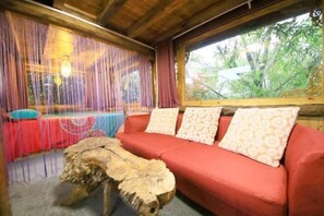 Quarto com sofá vermelho, mesa de centro de madeira e janela com cortinas.