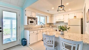 A modern kitchen with white cabinetry, granite countertops, and a central island with two white bar stools.
