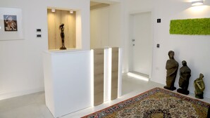 A modern interior with a white reception desk, a wooden panel wall, a green wall decoration, and a patterned rug. - Lo Studio di viale Lo Re Camere & Caffè  (Lecce)