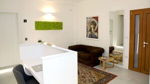 A modern living room with a white sofa, a small round table with books, a green wall art piece, and a painting of a woman. - Lo Studio di viale Lo Re Camere & Caffè  (Lecce)