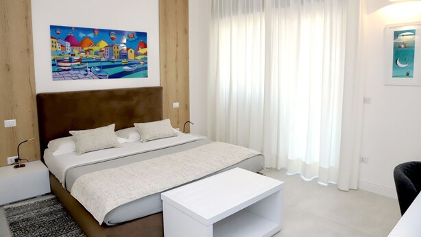 A bedroom with a bed, a bedside table, a nightstand, a painting, and a window with curtains. - Lo Studio di viale Lo Re Camere & Caffè  (Lecce)