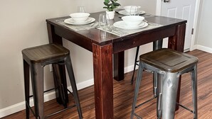 A dining table with four chairs, a framed painting on the wall, and a door in the background. - Tower Grove Studio - Fenced Yard, W/D, Pet-Friendly - 4 Mi to Downtown (St. Louis)