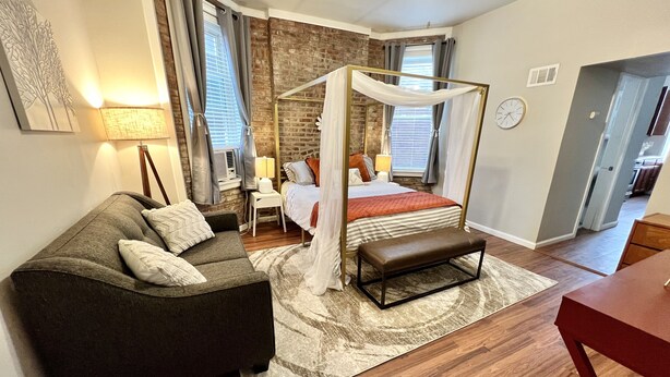 A modern bedroom with a four-poster bed, a sofa, a bench, and a dining table. - Tower Grove Studio - Fenced Yard, W/D, Pet-Friendly - 4 Mi to Downtown (St. Louis)