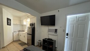 Una camera compatta con un letto, un angolo cottura, una TV a parete e una porta.
