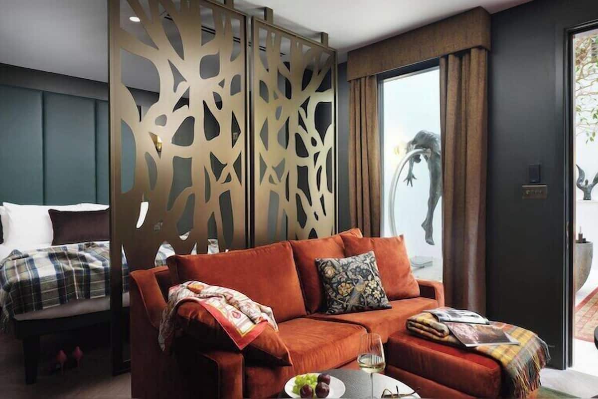 A modern hotel room with a red sofa, a bed with a plaid blanket, and a decorative screen.