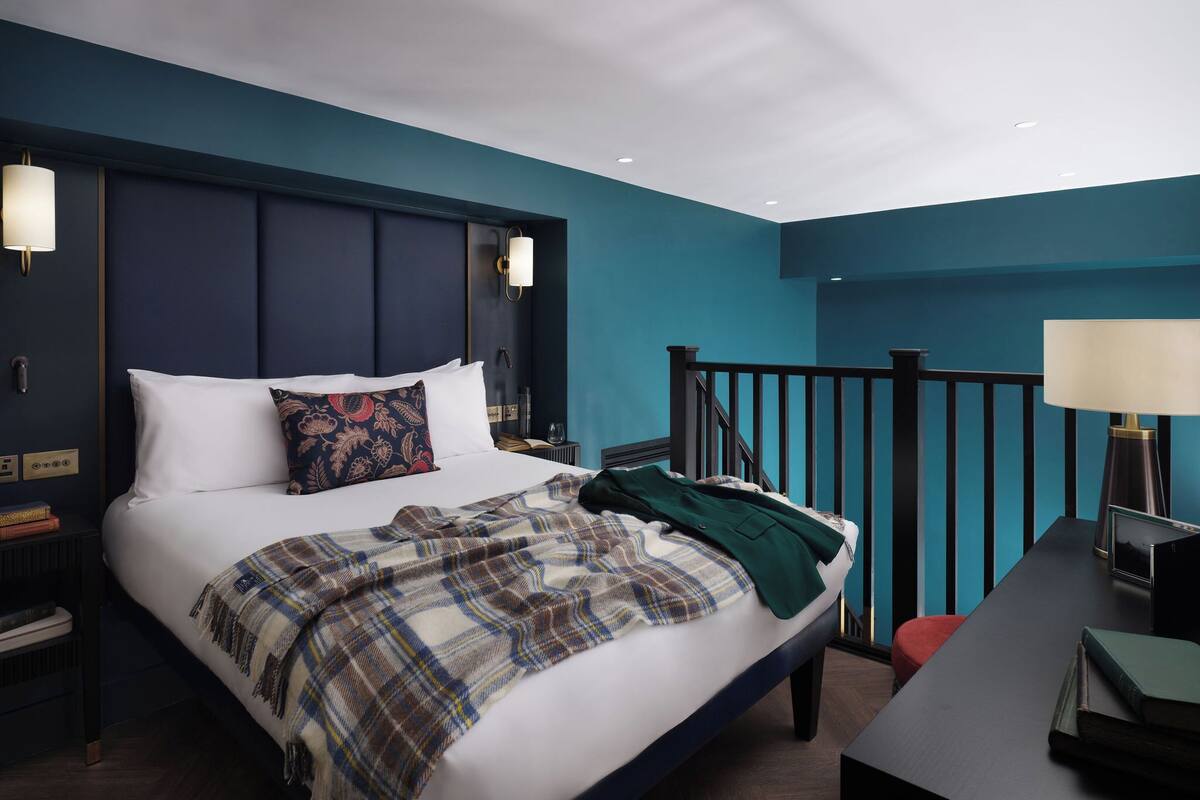 A modern hotel room with a large bed, a nightstand, a desk, and a staircase.