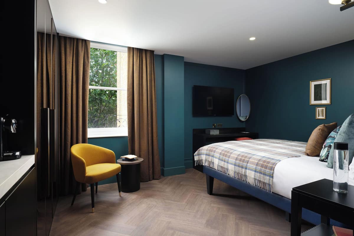 A hotel room with a bed, a desk, a chair, a TV, and a window with curtains.