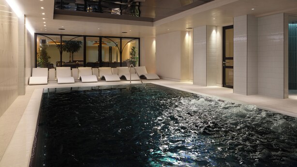 An indoor swimming pool with lounge chairs and a glass ceiling. - The Other House South Kensington (London)