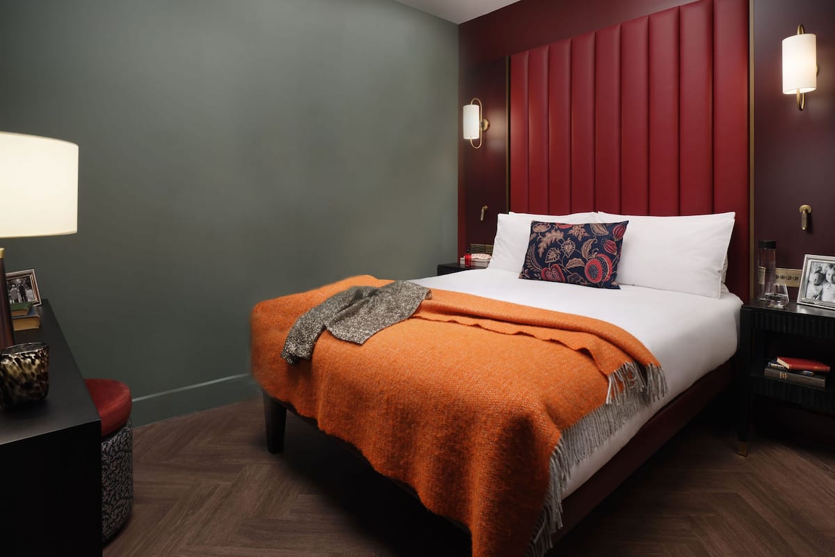 A hotel room with a bed, a nightstand, a lamp, and a wall-mounted light fixture.