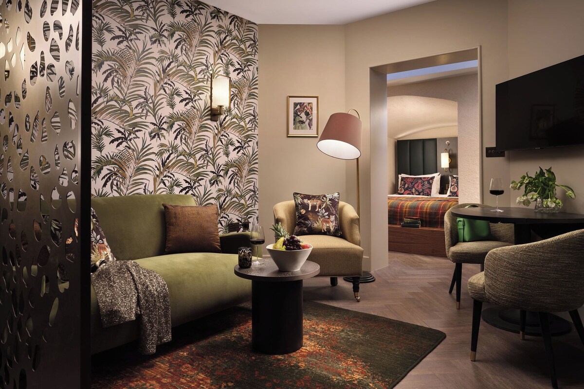 A modern living room with a sofa, armchair, and coffee table, a dining area with a TV, and a bedroom with a bed and nightstand.