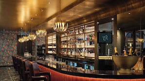 A bar area with a curved counter, multiple bar stools, and a variety of bottles and glasses on shelves. - The Other House South Kensington (London)