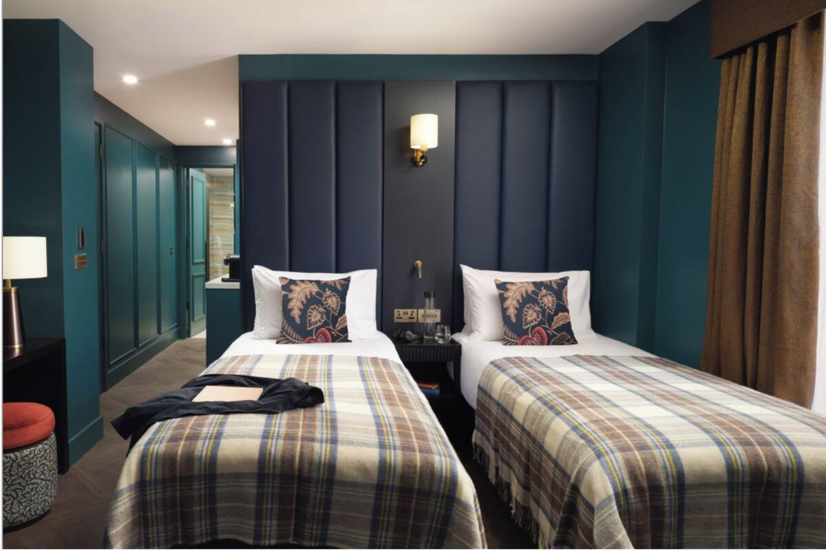 A hotel room with two beds, a nightstand, a lamp, and a view of the hallway.