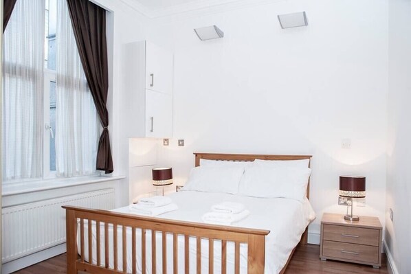 Ein Schlafzimmer mit einem Holzbett, weißer Bettwäsche, zwei Nachttischen mit Lampen, einem Fenster mit Vorhängen und einer Heizung.