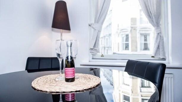 Une table à manger avec une bouteille de vin, deux verres et un set de table en fibres tressées.