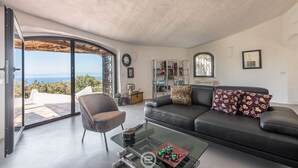 A modern living room with a glass coffee table, a black leather sofa, and a view of the outdoors. - Spectacular Seaview Escape (Quartu Sant'Elena)