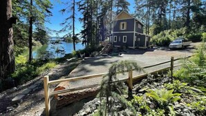 A two-story cabin with a dock, surrounded by dense forest and a lake.