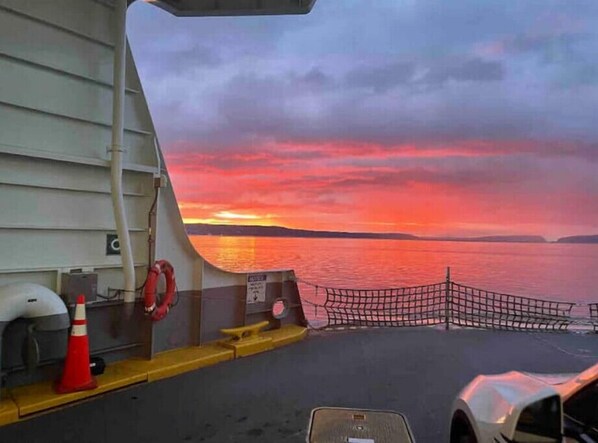 Vista del atardecer desde la cubierta de un barco, con un flotador salvavidas, un cono de tráfico rojo y una zona con redes.