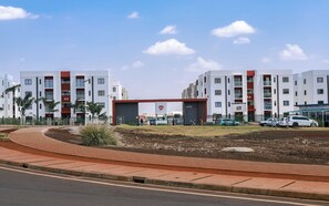 A modern building with multiple floors, a gated entrance, and a landscaped area with a pathway. - Cozy 2-BR Aprt with Pool, Gym at Tatu City (Kiambu County)
