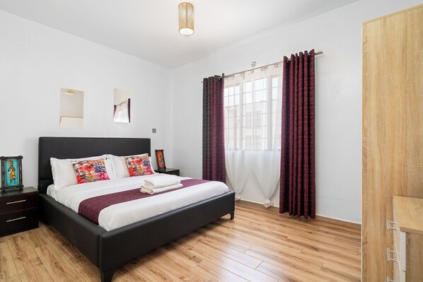 Een moderne slaapkamer met een zwart bed, houten vloer, een raam met gordijnen en een houten garderobe.