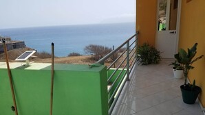 Un balcón con vistas al mar, una puerta y plantas en macetas.