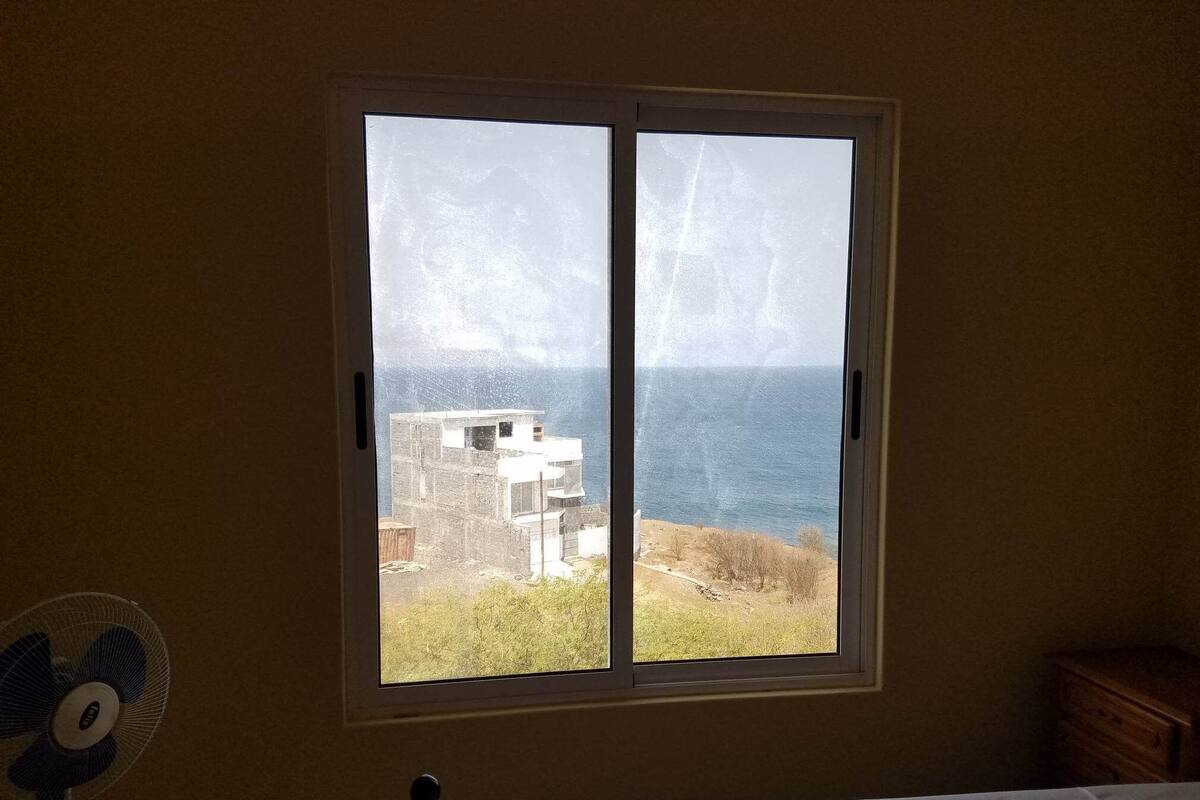 A bedroom with a large window overlooking a building and a body of water.