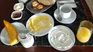 Una mesa de desayuno con pan, huevos, fruta y bebidas.