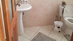 Un baño con lavamanos blanco, inodoro y un pequeño cubo de basura.