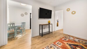 A hallway with a wooden floor, a TV mounted on the wall, a small table with a vase, and a patterned rug. - Salmon River Cabin #212 (Riggins)