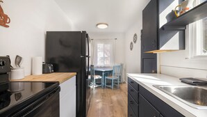 A compact kitchen with a black refrigerator, a wooden countertop, a sink, and a dining area with blue chairs. - Salmon River Cabin #212 (Riggins)