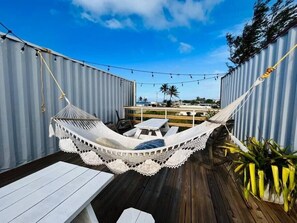 Una silla hamaca con funda de encaje blanco, terraza de madera y paredes metálicas.