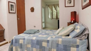 A bedroom with a bed, a wooden door, a framed picture, and a window with curtains.