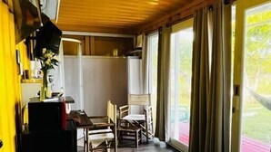 Ein Zimmer mit einem Bett, einem Schreibtisch und einem Stuhl. Ein Fenster mit Vorhängen bietet Blick ins Grüne.