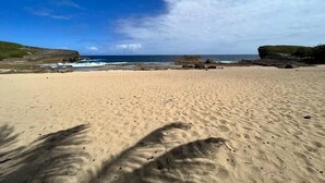 Ein sandiger Strand mit Felsformationen und wolkenlosem, blauem Himmel.