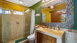 Un bagno moderno con box doccia in vetro, un WC, un lavabo con mobiletto in legno e uno specchio decorativo con cornice lavorata.