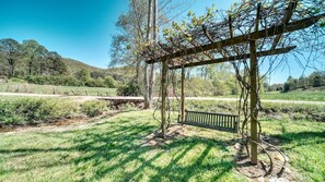 A wooden pergola with a bench in a grassy field with a stream and trees in the background. - Country Lane - Creek Front (Hiawassee)