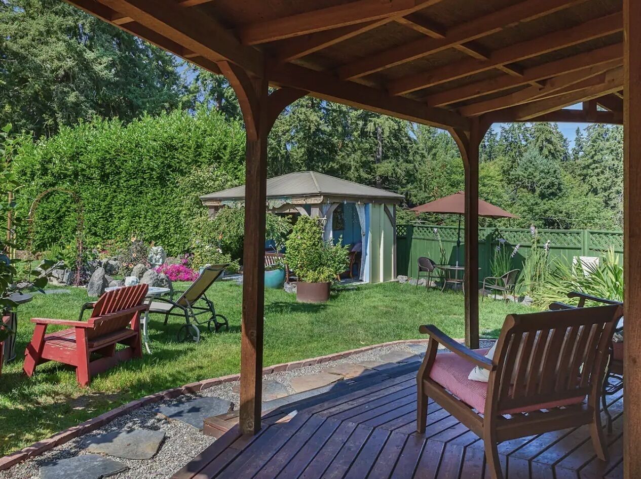 A covered patio area with wooden furniture, a small shed, and a garden with various plants and a lawn.