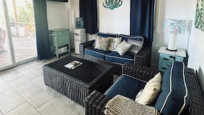 Een woonkamer met een bank, salontafel en een televisie. Er is een cactusdecoratie aan de muur en een waterdispenser.