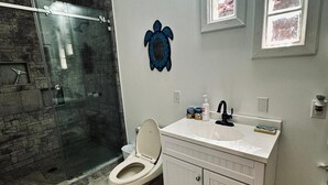 Een badkamer met een douchecabine van glas, een toilet, een wastafel met spiegel erboven en decoratieve wanddecoratie van een schildpad.