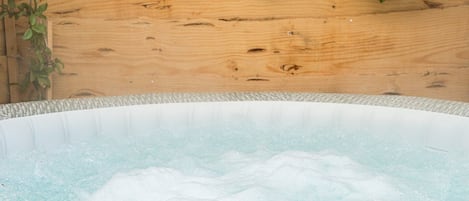 A hot tub with a wooden backdrop and green foliage.