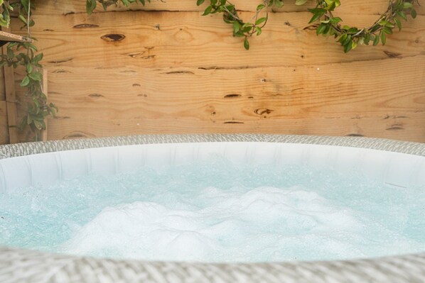 A hot tub with a wooden backdrop and green foliage.
