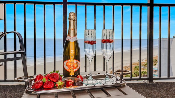 Un balcón con vistas a la playa, una botella de Chandon, dos copas, fresas y bombones en una bandeja.
