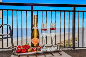 A balcony with a view of the beach, a bottle of Chandon champagne, two glasses, strawberries, and chocolates on a tray. - Make Memories @ Ravishing Angled Oceanfront Suite (Myrtle Beach)