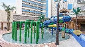 Un área de parque acuático con una estructura de juegos, palmeras y una piscina.