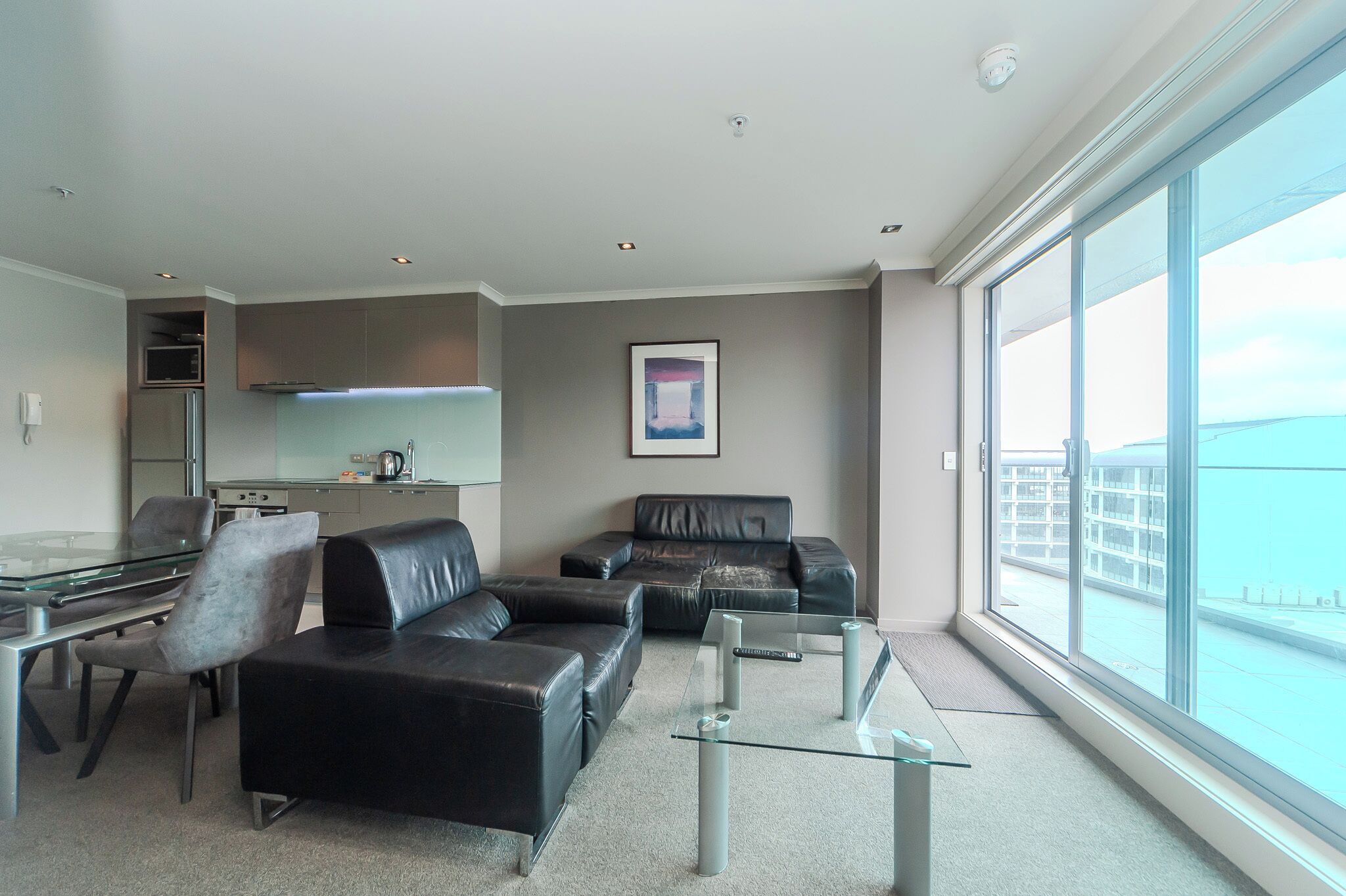 A modern living room with a glass coffee table, leather sofa, and a dining area with a glass table and chairs.